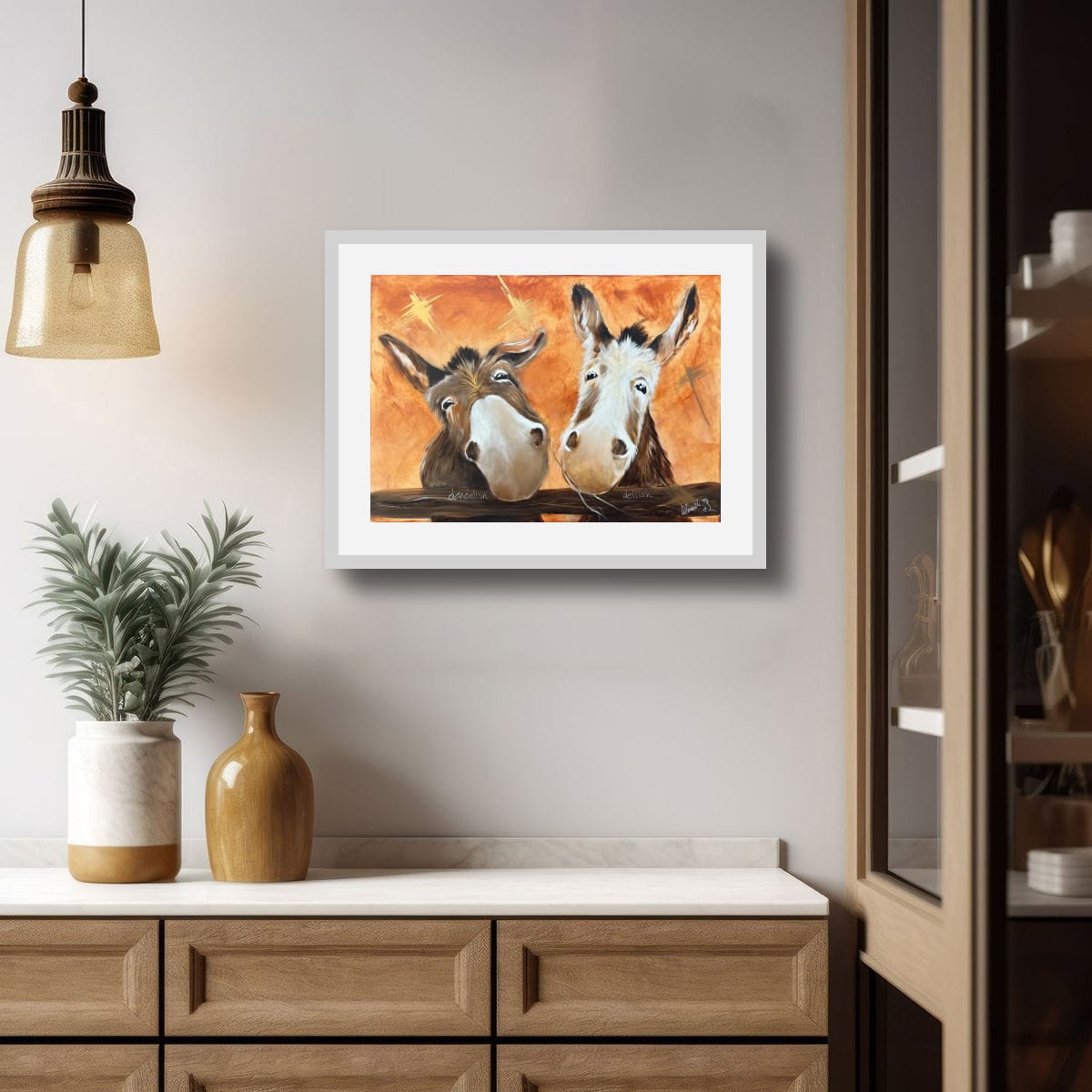 “Framed print of Dandelion and Delilah, a painting of two donkeys in warm orange tones, shown in a styled interior setting.”